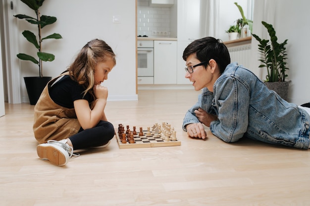 Supportive dad teaching chess to his child daughter they play on the floor