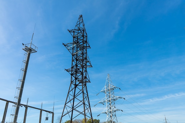 Supports high-voltage power lines against the blue sky with clouds. Electrical industry.