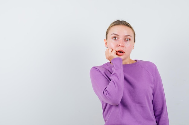 The suprised blonde woman is holding her hand on cheek on white background