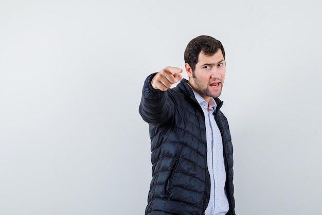 The suprised young man is pointing to camera with forefinger on white background