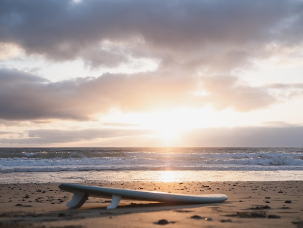 Surfboard lying on the beach and the sunrise in a cloudy sky