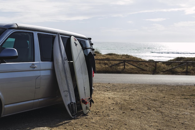 Surfboards leaning on a van on the road surrounded by the sea under the sunlight