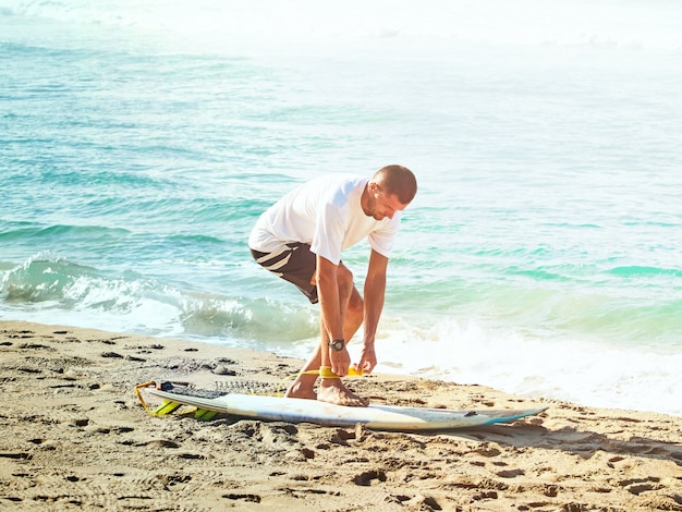 Surfer gets on a surf leash. Sandy beach by the atlantic ocean.