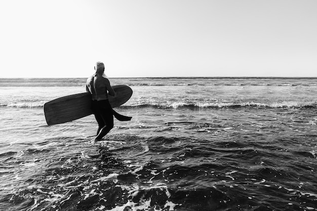 Surfer senior man having fun while surfing on beach with vintage surf board  Focus on male back  Black and white edition