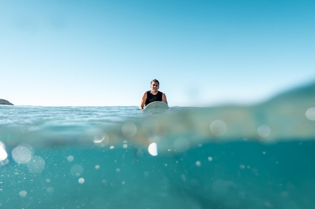 Surfer Sitting on His Board Looking to the Camera in a Sunny Day Split ShotWater Sport Concept