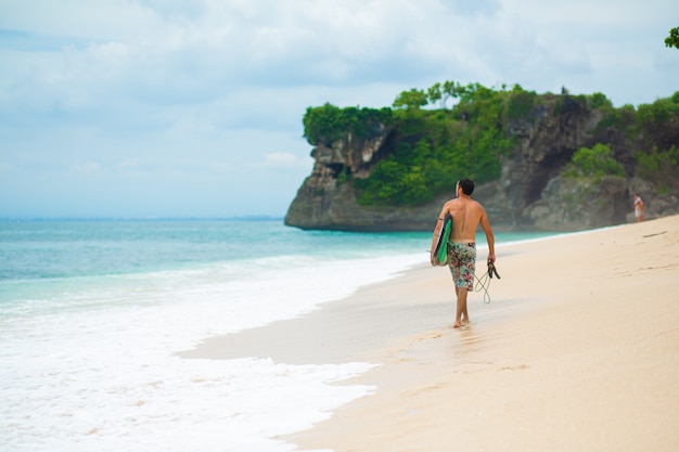 Surfer. Surfing Man With Surfboard Walking On Sandy tropical Beach. Healthy Lifestyle, water activities, Water Sport. Beautiful Ocean