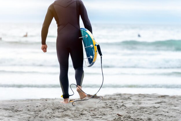 Surfer walking on the sand carrying the surfboard about to enter the sea.