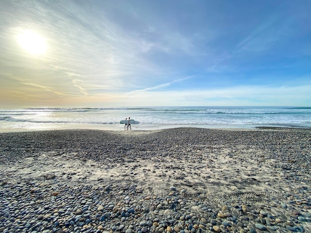 Surfer walking with their boards on Torrey Pines State Beach before sunset twilight