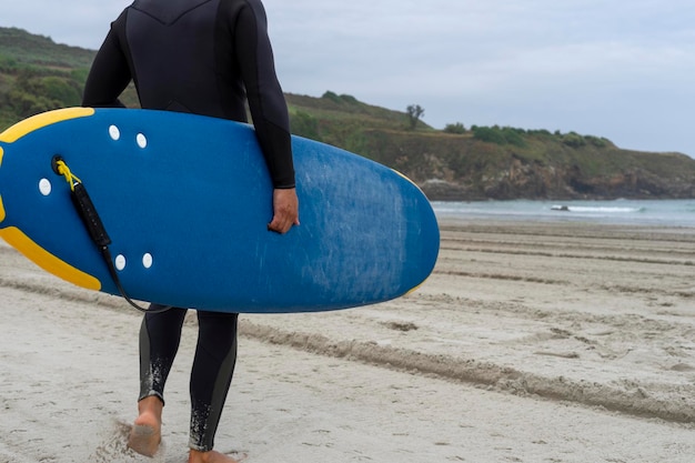 Surfer in wetsuit walks on the sand grabbing his surfboard to enter the beach and start surfing