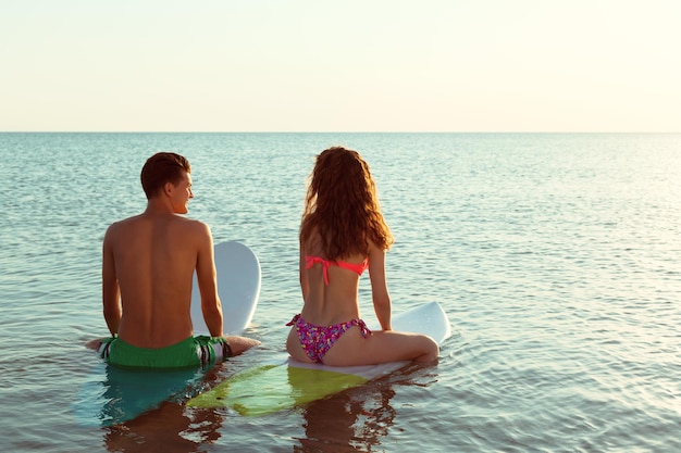 Surfing couple leaning on surfboards in sea