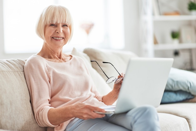 Surfing the net at home. Beautiful senior woman looking at camera and smiling 