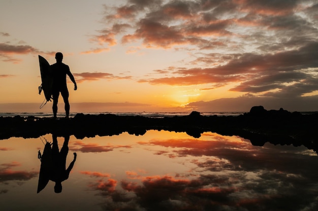 Surfing at sunset with reflection of sky on water