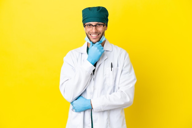 Surgeon blonde man in green uniform isolated on yellow background with glasses and smiling