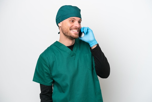 Surgeon Brazilian man in green uniform isolated on white background keeping a conversation with the mobile phone