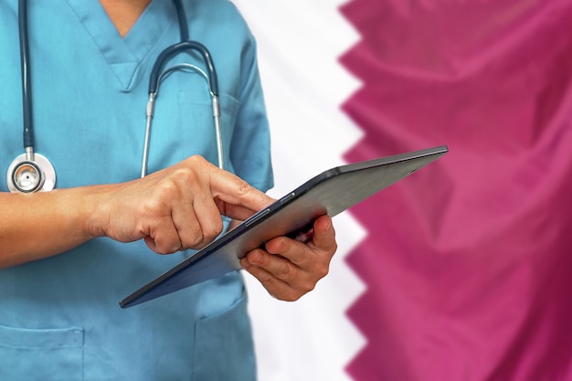 Surgeon or doctor using a digital tablet on the background of the Qatar flag