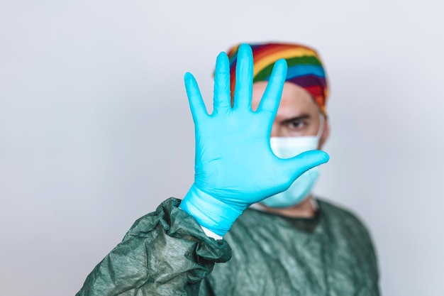 Surgeon doctor with protective mask and rainbow bandanna on his head who is showing his hand in blue glove Doctor stopping hiv virus or coronavirus with prevenction Lgbtq people rights concept