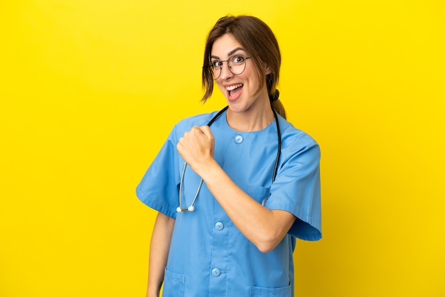 Surgeon doctor woman isolated on yellow background celebrating a victory