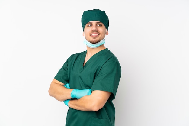 Surgeon in green uniform on isolated white wall with arms crossed and happy