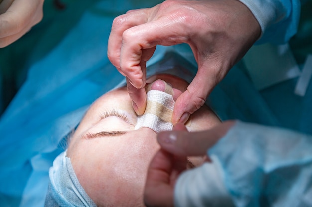 Surgeon and his assistant performing cosmetic surgery on nose in hospital operating room. Nose reshaping, augmentation. Rhinoplasty.