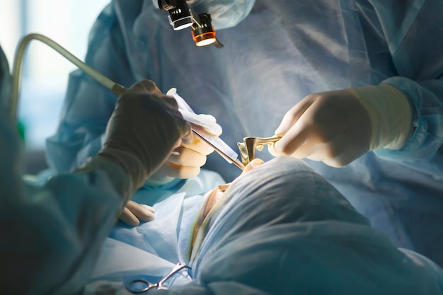 Surgeon and his assistant performing cosmetic surgery on nose in hospital operating room.