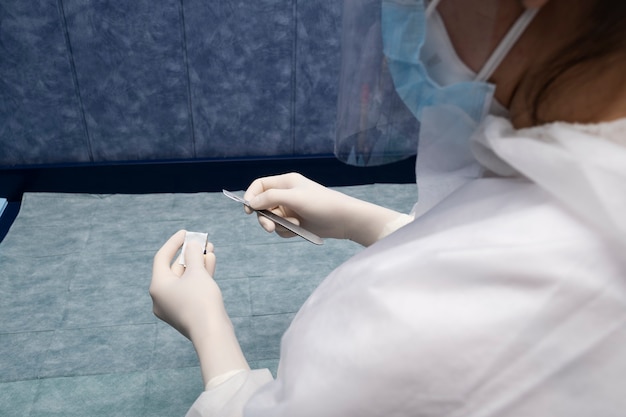 Surgeon holds scalpel dressed in a green surgical apron and mask on light background. Medical and pharmaceutical concept. Scalpel surgeon's scissors, just before surgery. Responsible work of surgeon.