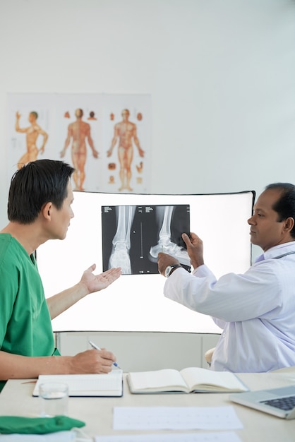 Surgeon and radiologist discussing heel fracture treatment and pointing at feet x-ray image on wall