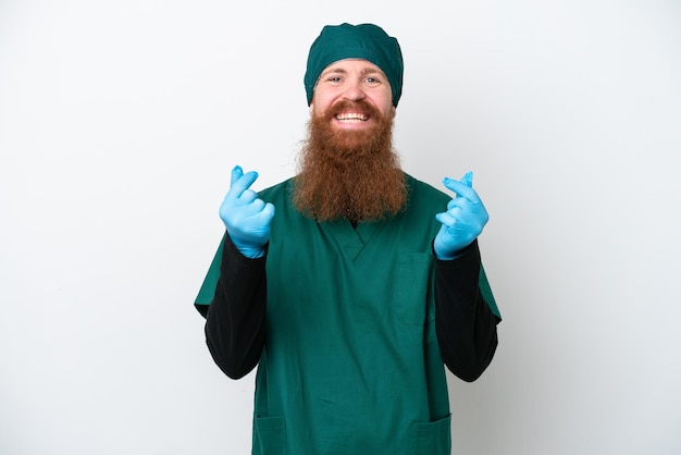 Surgeon redhead man in green uniform isolated on white background making money gesture