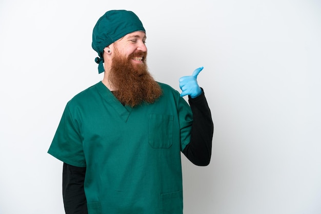 Surgeon redhead man in green uniform isolated on white background pointing to the side to present a product