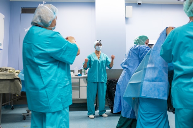 Surgery, medicine and people concept - group of surgeons in operating room at hospital talking and preparing to operation