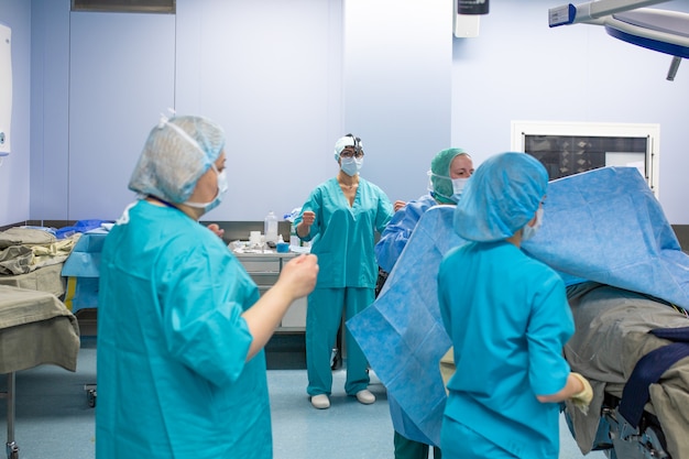 Surgery, medicine and people concept - group of surgeons in operating room at hospital talking and preparing to operation