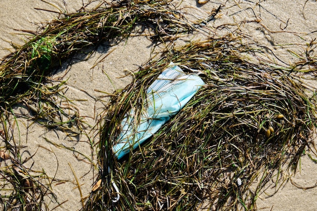 Surgical mask dumped on the beach, pollution concept