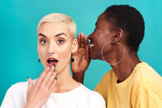 Photo surprise secret shock and girl friends portrait with privacy laugh and gossip in a studio blue background women and smile of a female person with whisper and news telling a story and listening