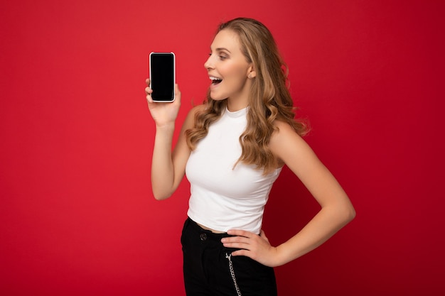 Surprised amazed beautiful young blonde woman wearing white t-shirt isolated on red background with