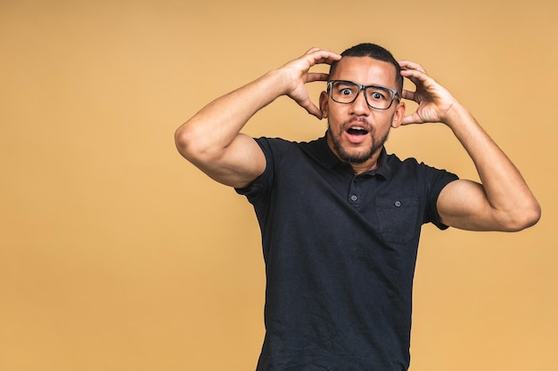 Surprised amazed shocked african american man guy in casual isolated over beige background studio portrait People lifestyle concept Mock up copy space Keeping mouth open