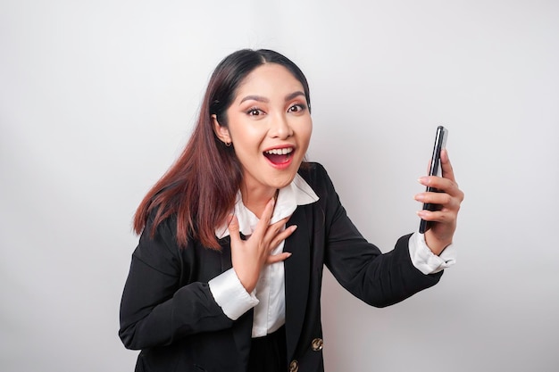 Surprised Asian businesswoman wearing black suit holding her smartphone isolated by white background