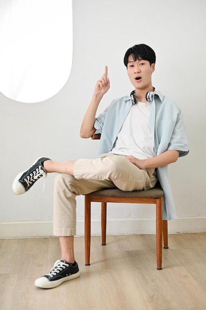 Surprised Asian man in casual clothes sits on a chair showing a finger making surprising face