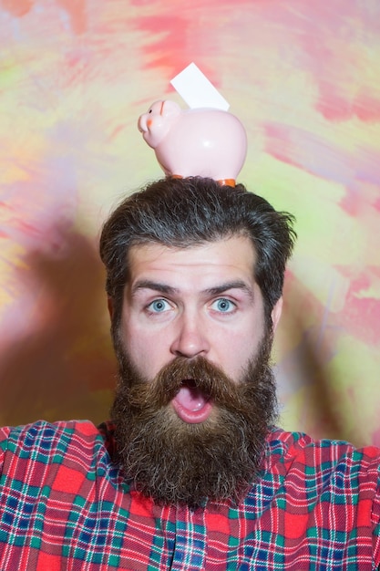 Surprised bearded man with pink ceramic piggy bank on head