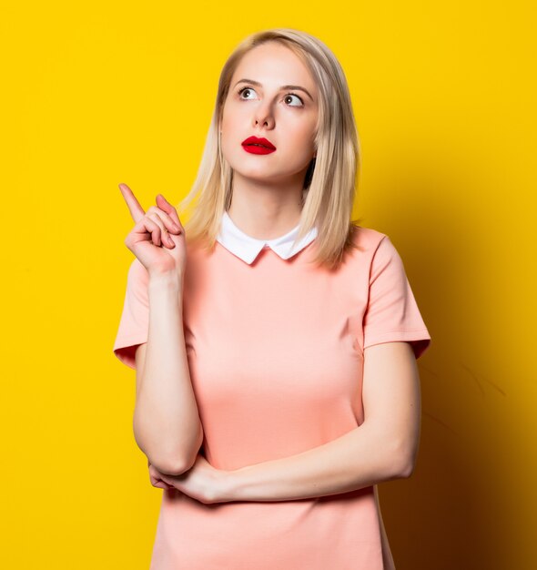 Surprised blonde girl in pink dress on yellow space