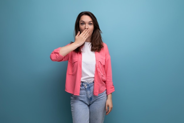 Surprised brunette young woman with shoulderlength hair in a pink shirt covered her mouth with her