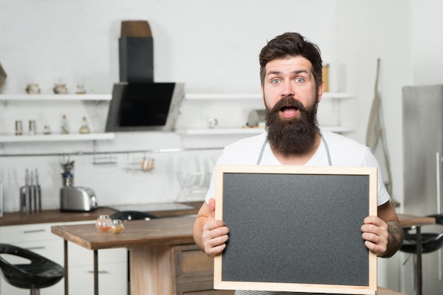 Surprised brutal bearded man chef hold blank board for copy space offer