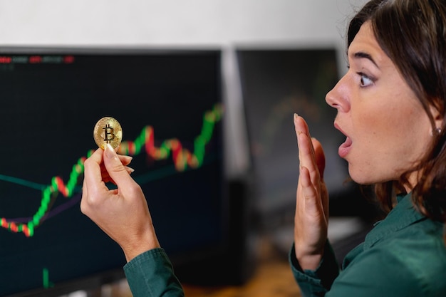 Surprised business woman holding and looking a bitcoin coin. Trading online, virtual money and cryptocurrency