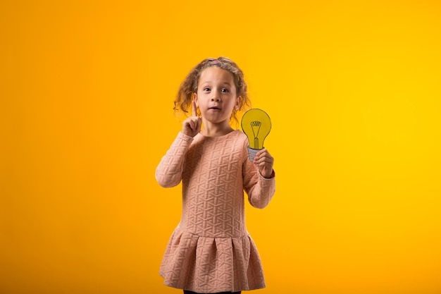 Surprised child girl holding paper bulb and pointing finger up Success motivation winner genius idea concept