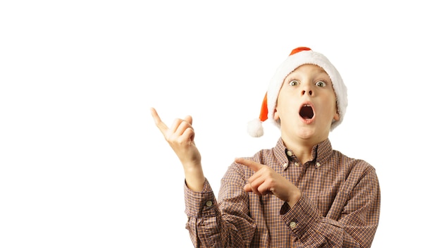 Surprised child in Santa Claus hat points fingers at an invisible object, isolated on white background. christmas banner mockup