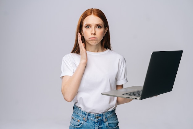 Surprised displeased young woman student holding keeping opened laptop and looking at camera