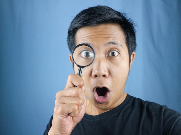 Surprised Expression asian man looking through magnifying glass searching or investigating something