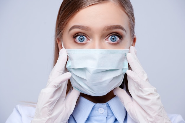 Surprised female doctor face in protective mask and nitrile medical gloves.