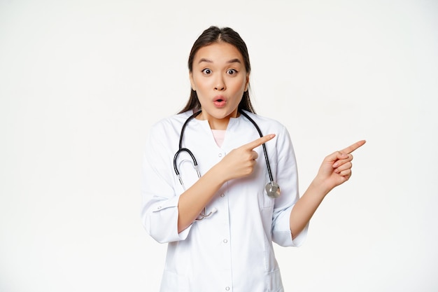 Surprised female doctor say wow pointing right and looking amazed with discounts in clinic showing w...