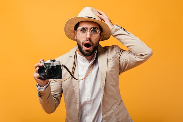 Surprised guy in hat and beige outfit holding retro camera