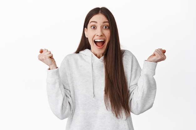 Surprised happy girl winning prize achieve goal gasping amazed and jumping from happiness and overjoy celebrating great news become champion receive award standing over white background