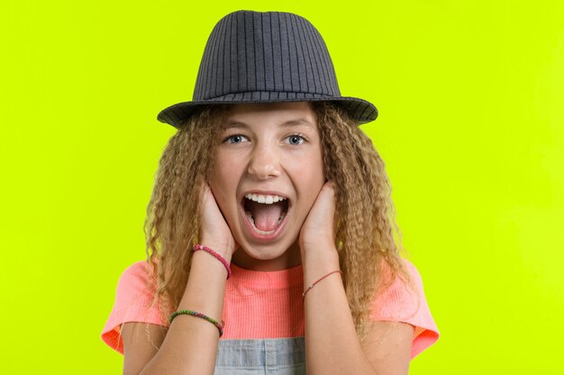 Surprised happy teen girl with curly hair in hat looking at the camera